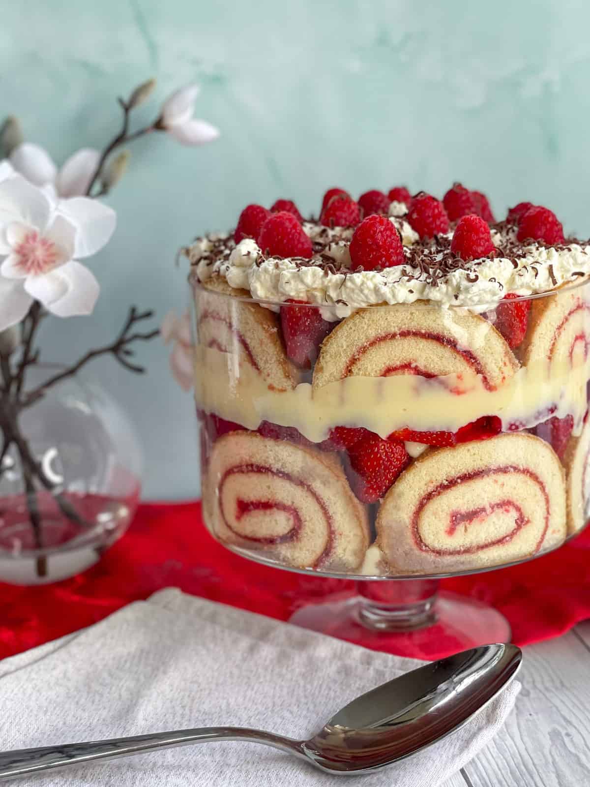 Large classic trifle with berries and sponge roll and a large silver serving spoon