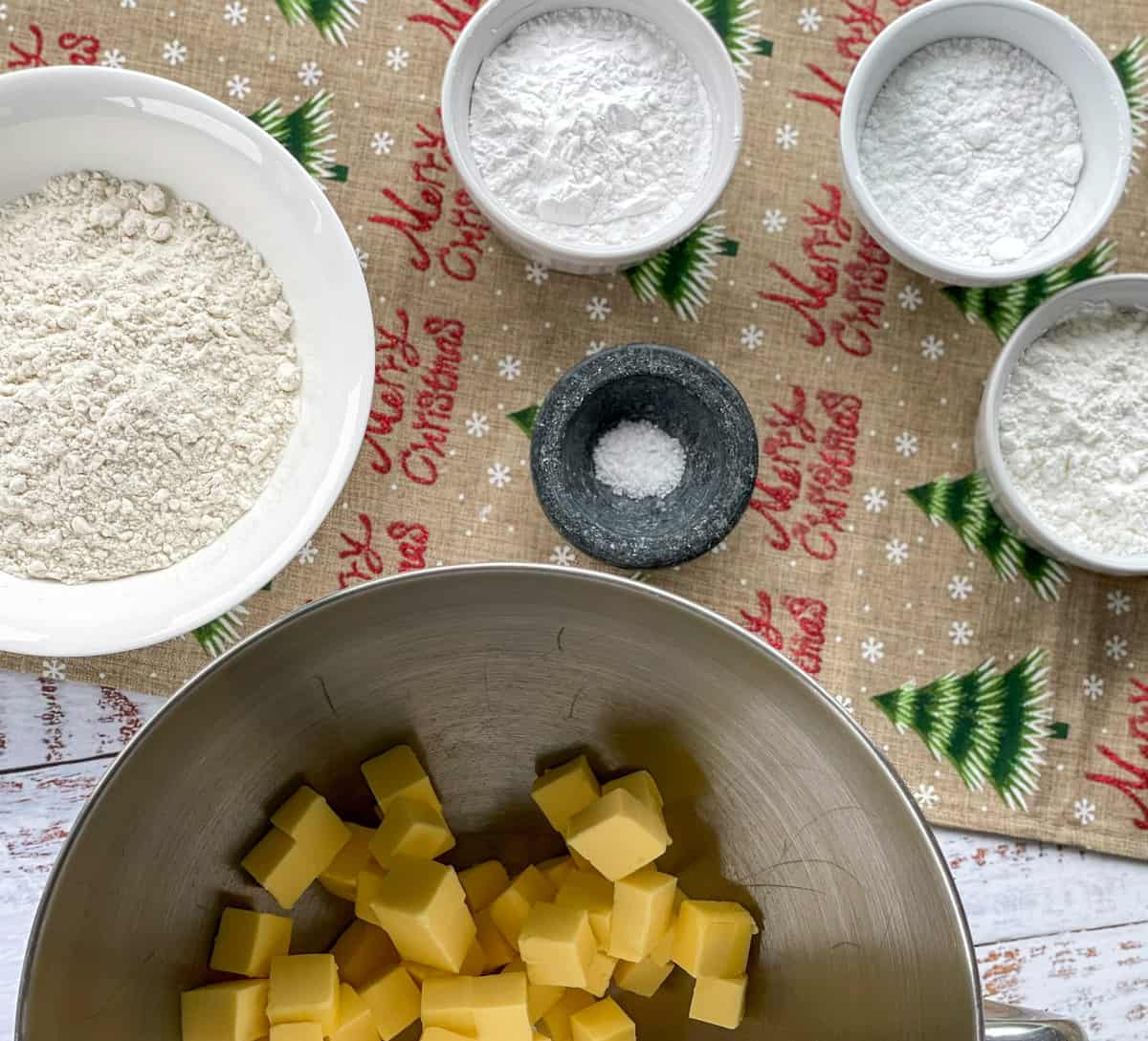 Small bowls of ingredients and butter cubed into a mixing bowl 
