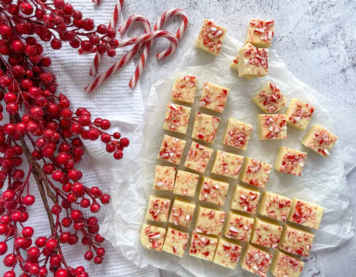 White chocolate peppermint fudge, candy canes and red berries on a white background 