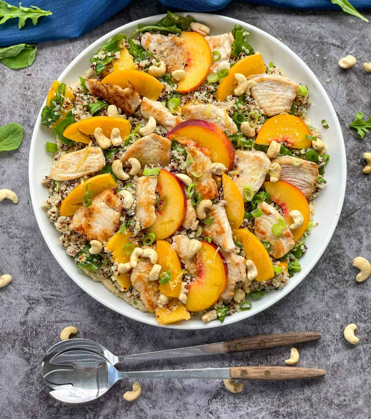 White platter with a chicken quinoa peach salad with rocket and cashews and serving spoons 