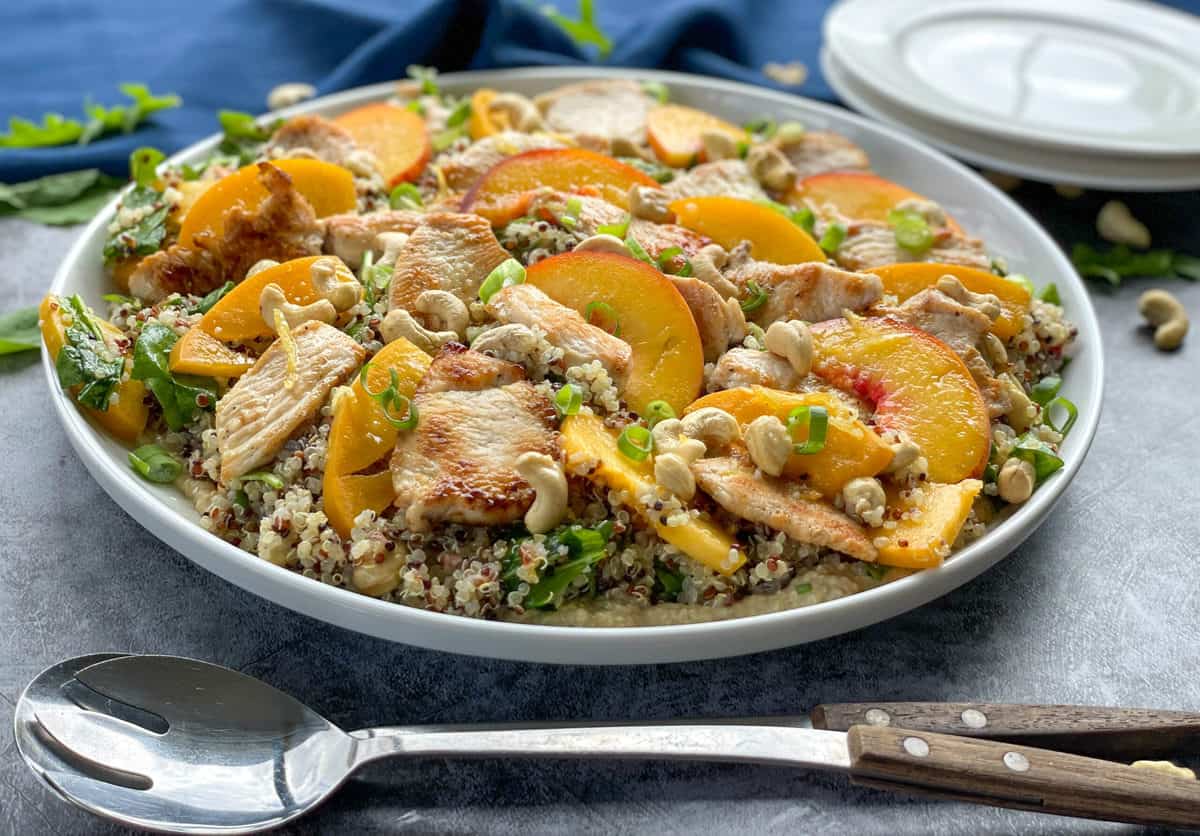 On a blue background a white platter with chicken quinoa and peach salad with a lemon dressing