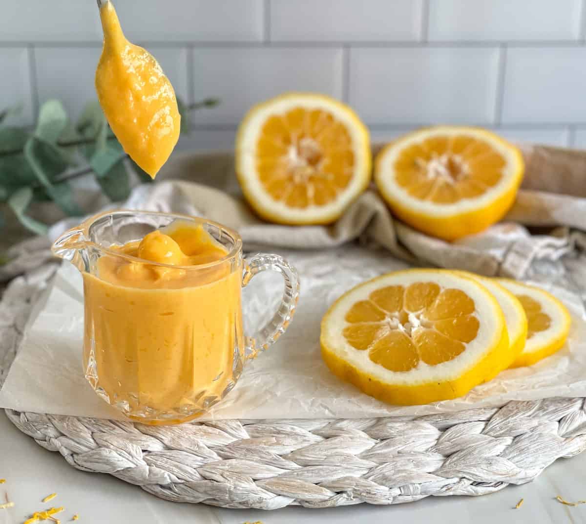 Lemon Curd thick and dripping off the spoon into a glass jar 
