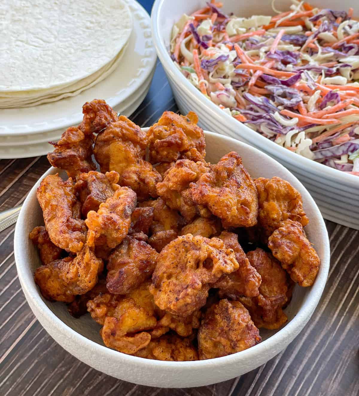 Bowl of deep fried karaage chicken in a white bowl with tortillas and coleslaw 