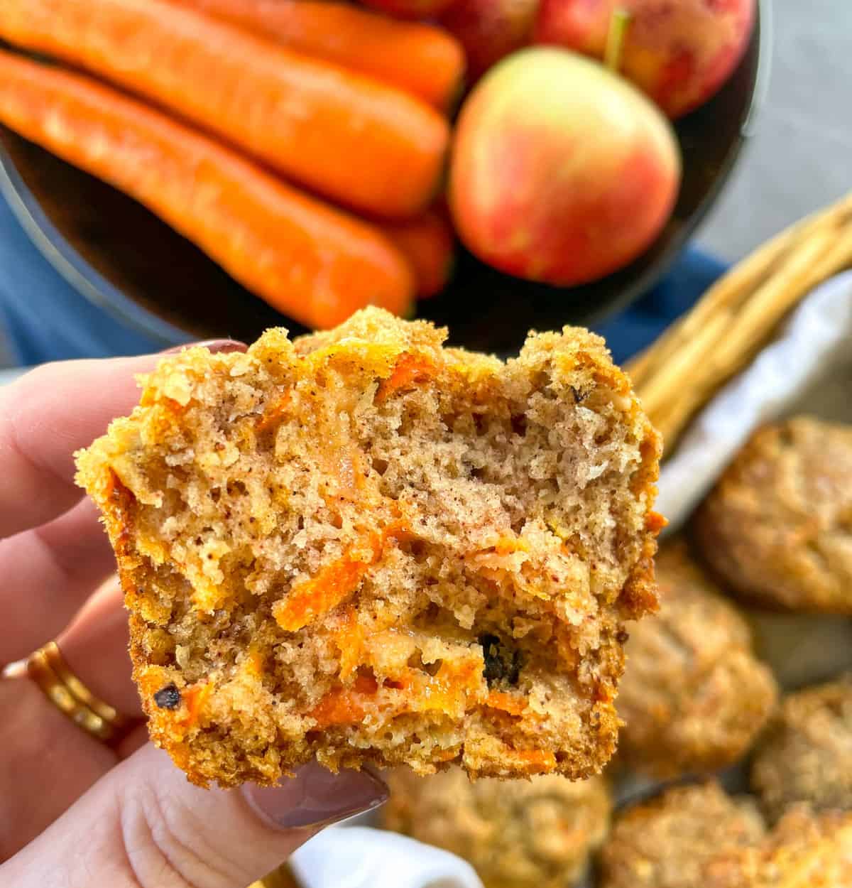 A hand holding half a apple and carrot muffin showing the moist loaded texture inside 