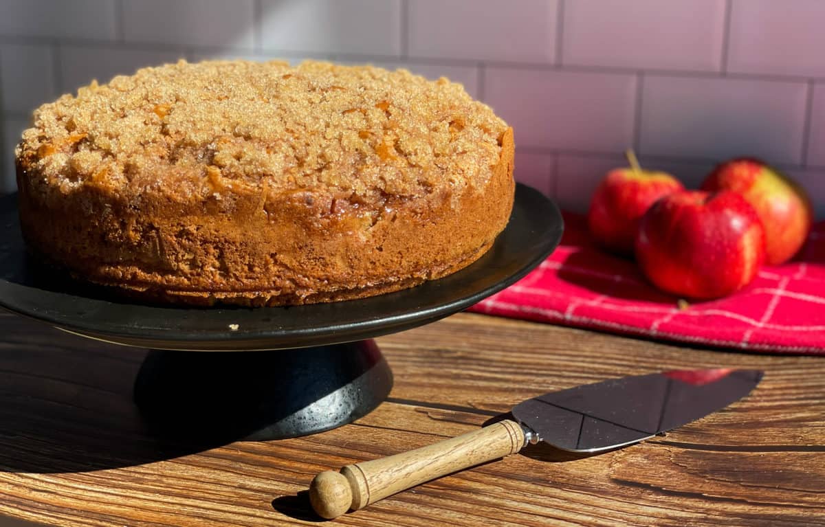 A Apple Crunch Cake on a black cake plate with a wooden knife