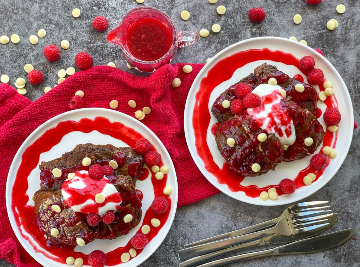 Two white plates with hot cross bun French Toast drizzled with raspberry coulis and white chocolate drops 