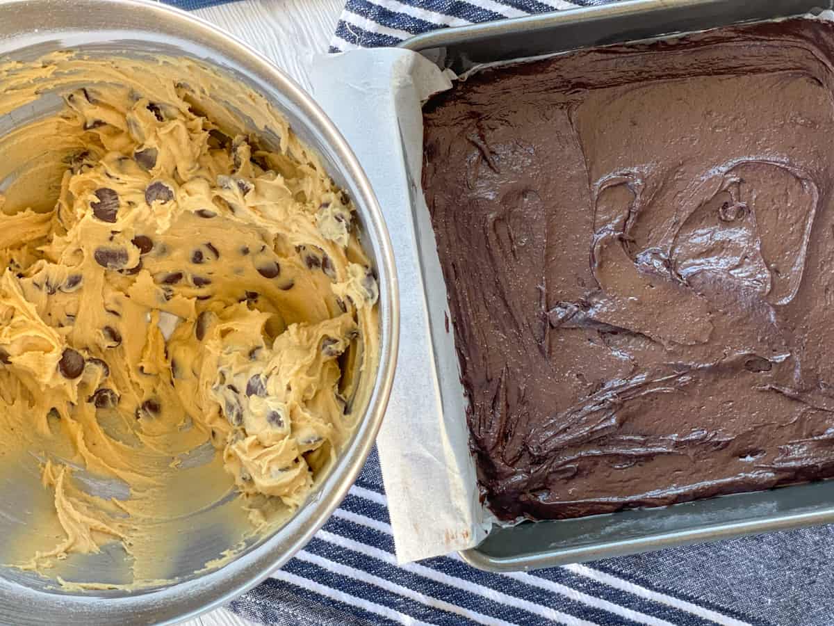 A bowl of cookie dough and a brownie mixture in the baking pan