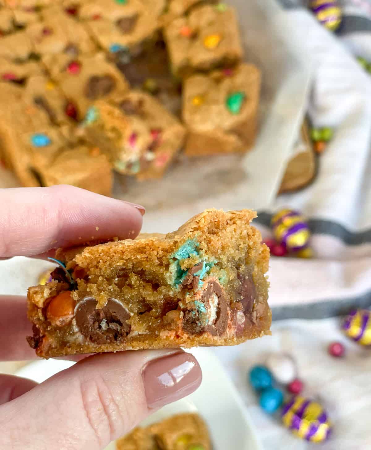 A hand holding a piece of Easter Cookie sliced filled with mini easter eggs