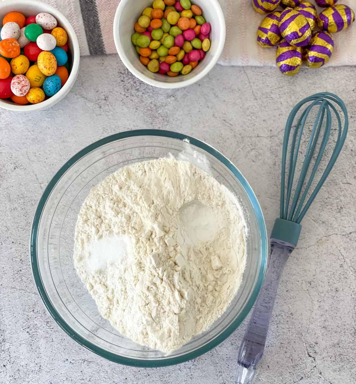 Combine the dry ingredients first, a bowl with flour, salt and baking soda with bowls of easter eggs nearby
