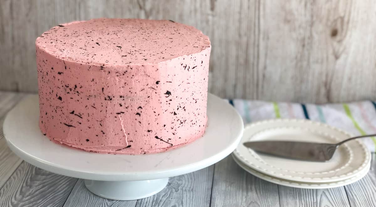 A pink cake with chocolate speckles on the outside on a white platter