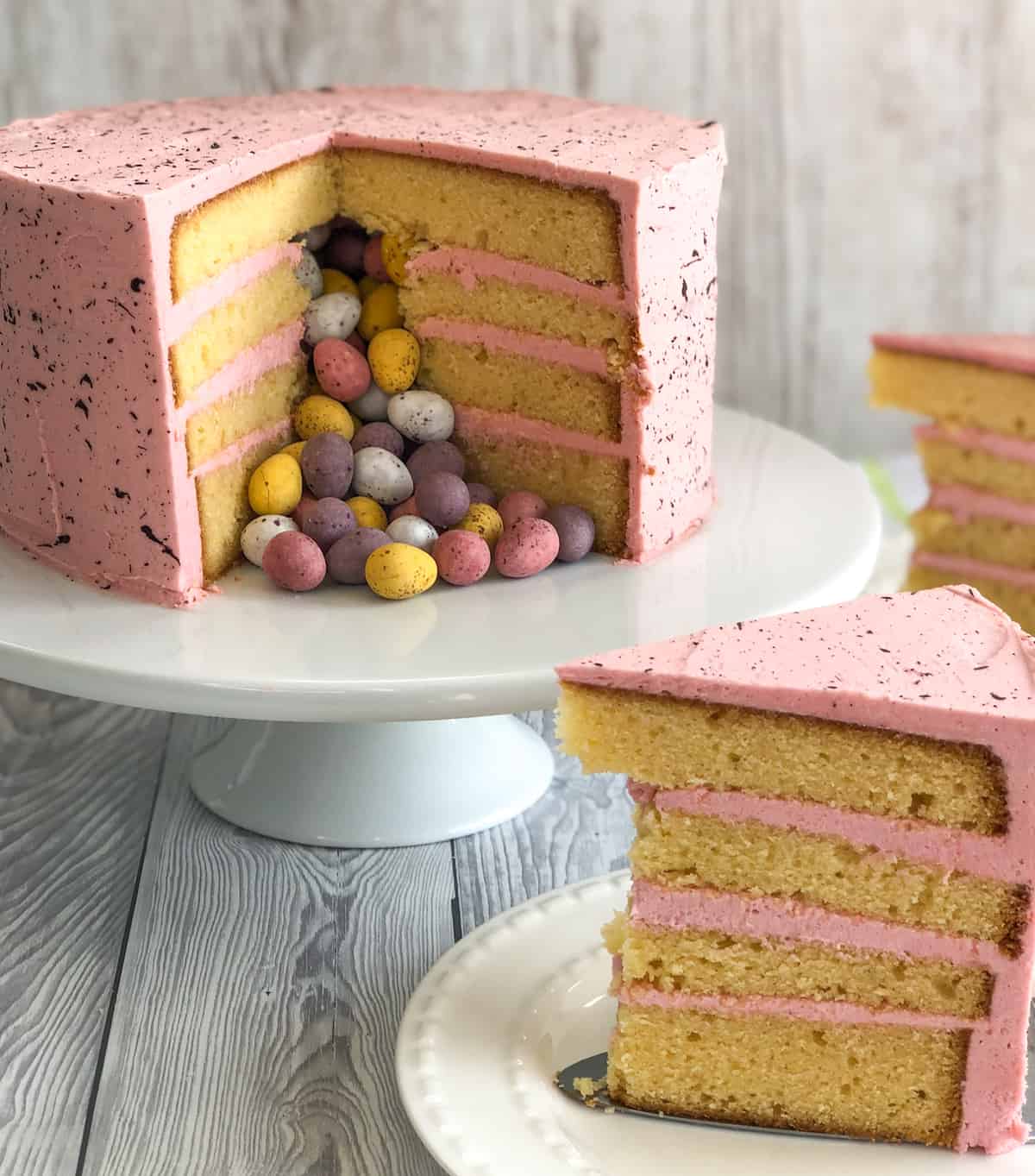 Slices of Easter layer cake, with white chocolate mudcake, pink buttercream and candy coated easter eggs
