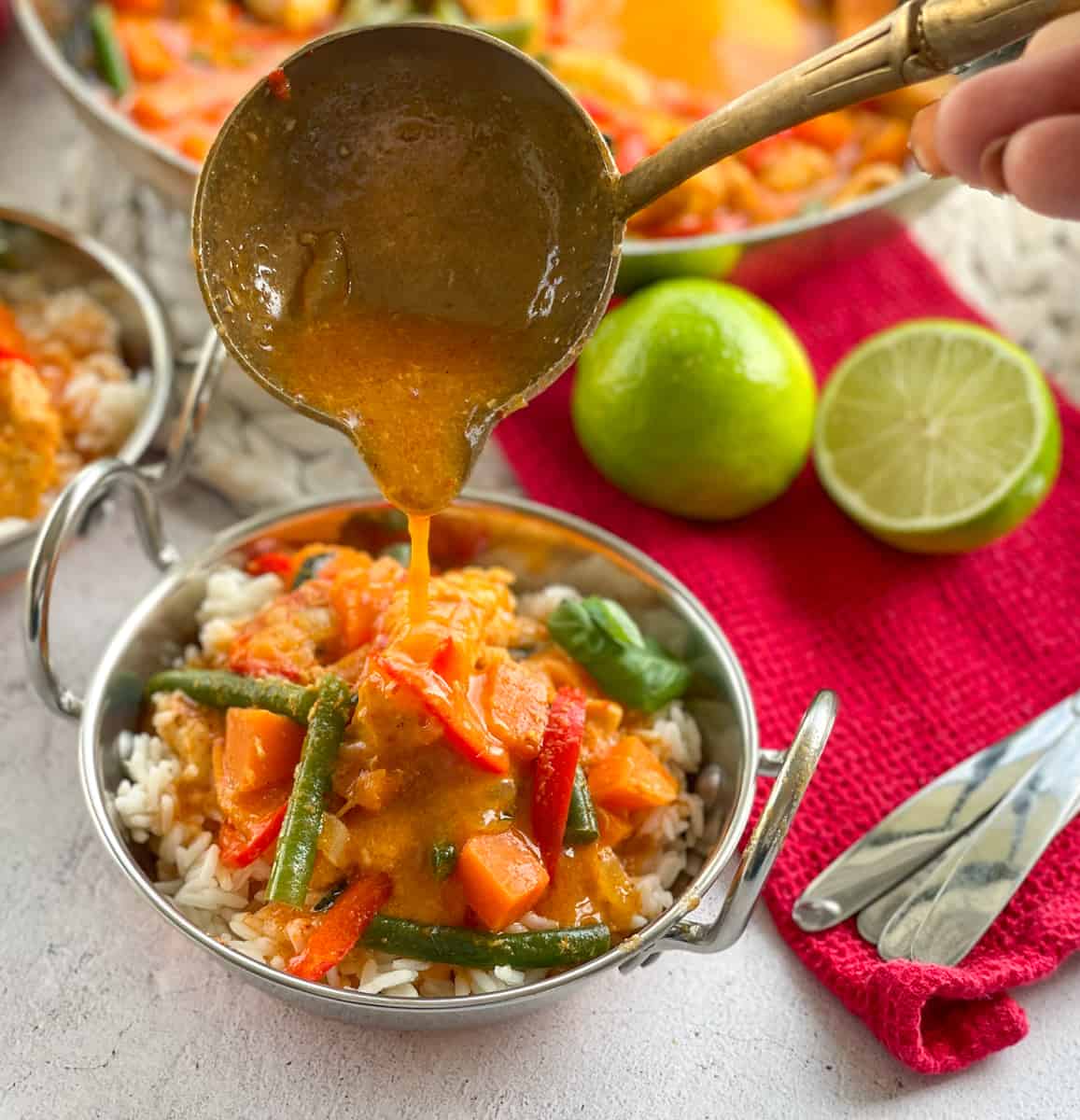 Chicken and Kumara Red Curry in a bowl. Ladle with curry sauce and limes