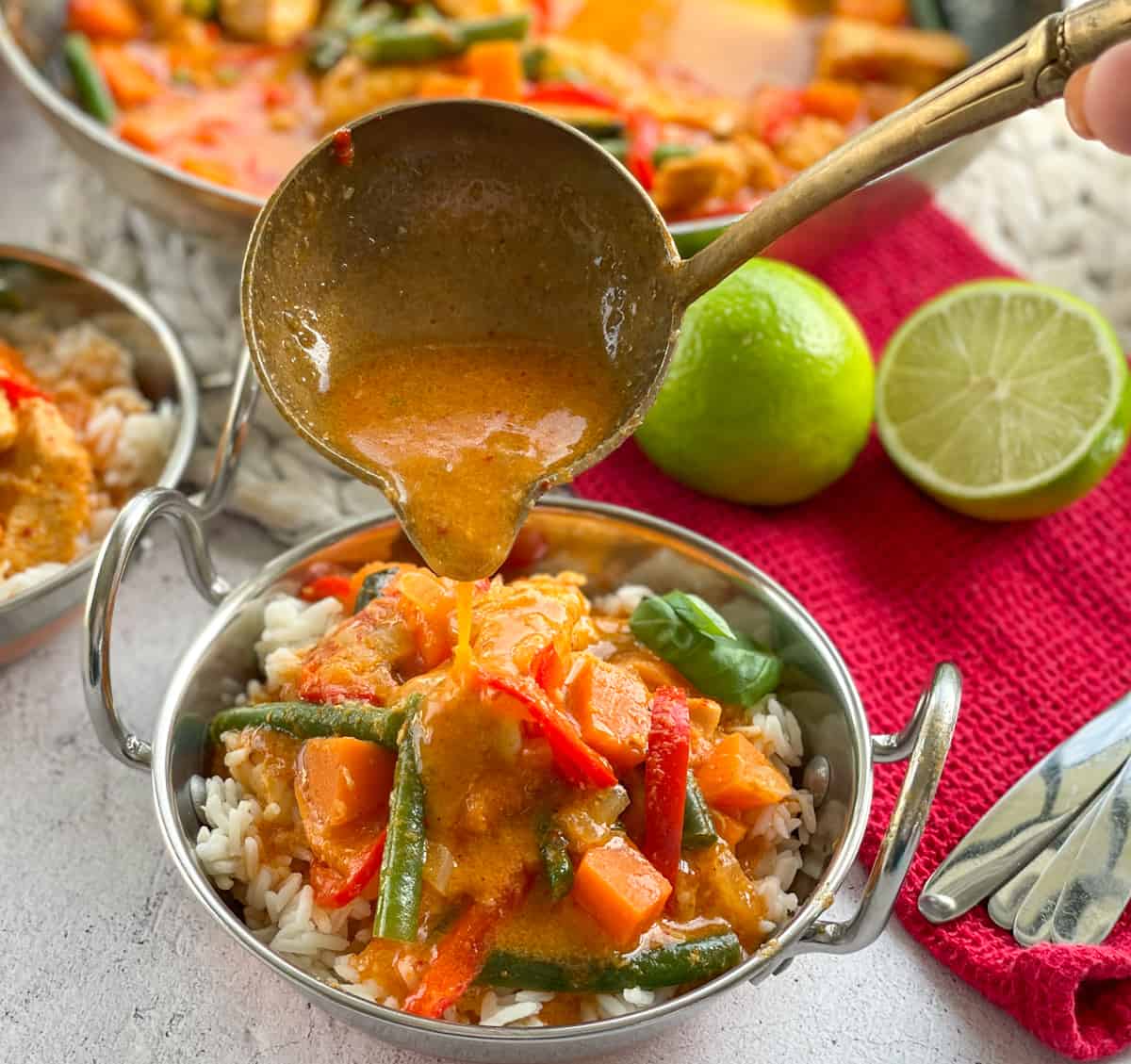 Pouring a ladle of red curry sauce over a bowl of chicken and kumara curry on rice