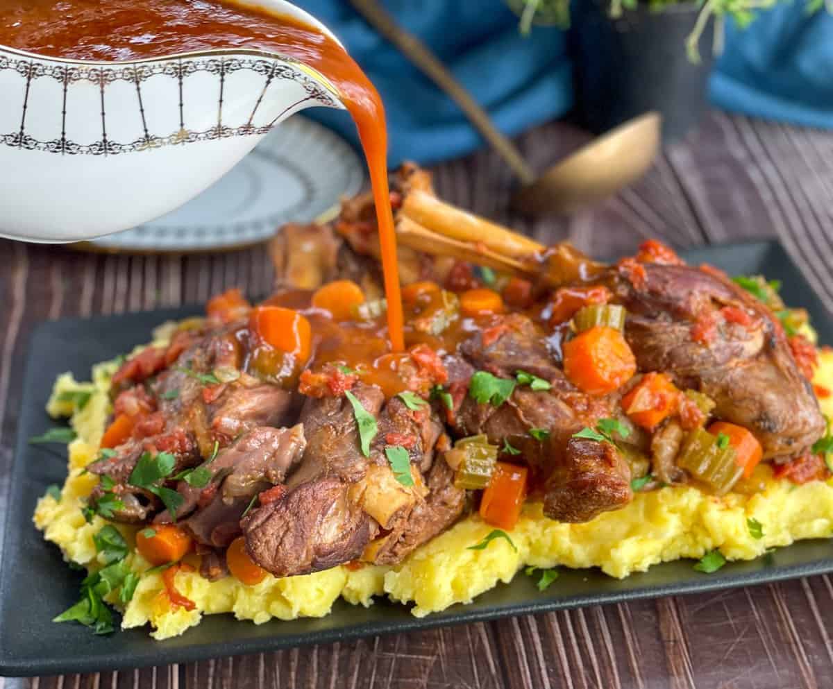 Pouring red wine sauce over lamb shanks 