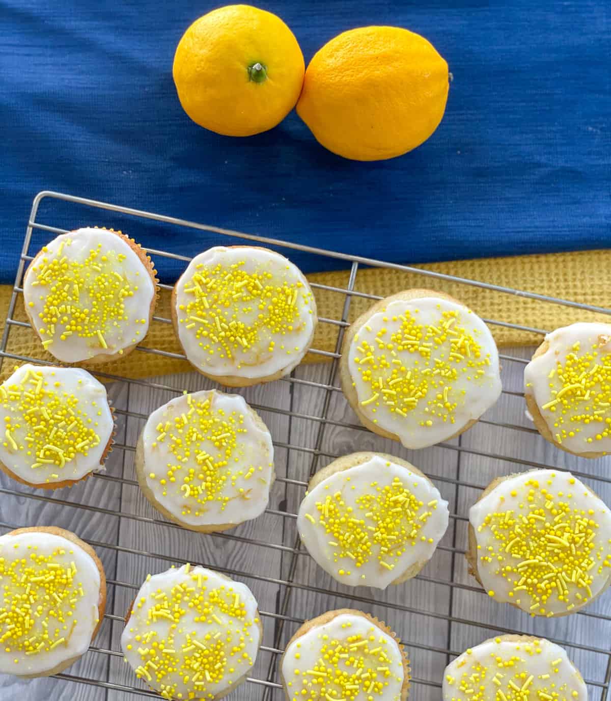 Freshly iced lemon cupcakes on a wire rack with fresh lemons in the background