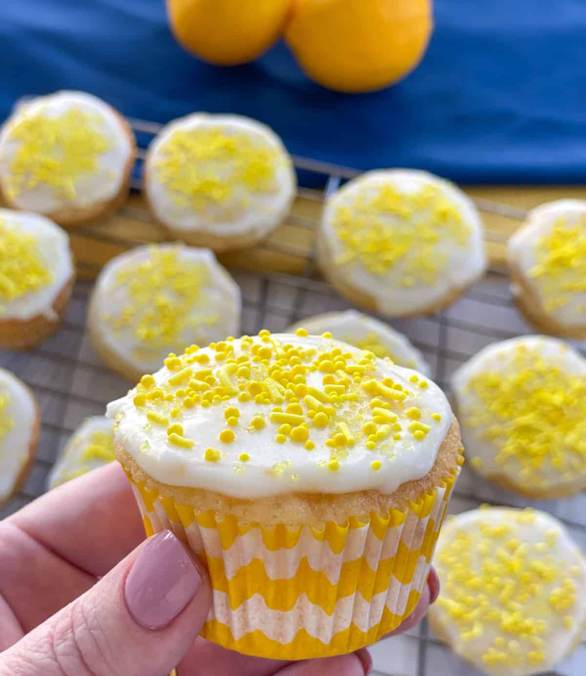 Hand holding a lemon cupcake with basic lemon icing, yellow cupcake cases and yellow sprinkles on top