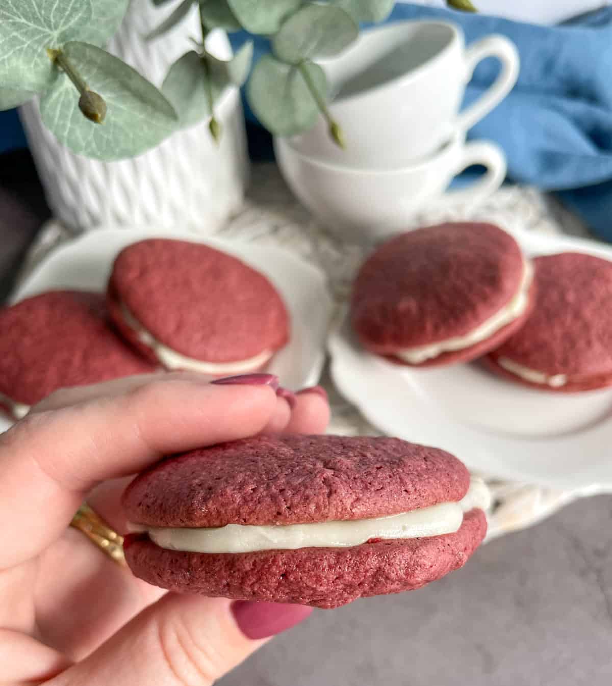 A hand holding a red velvet whoopie pie with frosting 