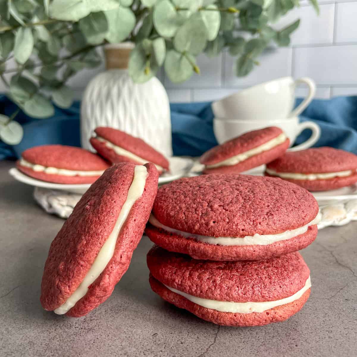 A stack of red velvet whoopie pies with cream cheese frosting in front of white and blue decor
