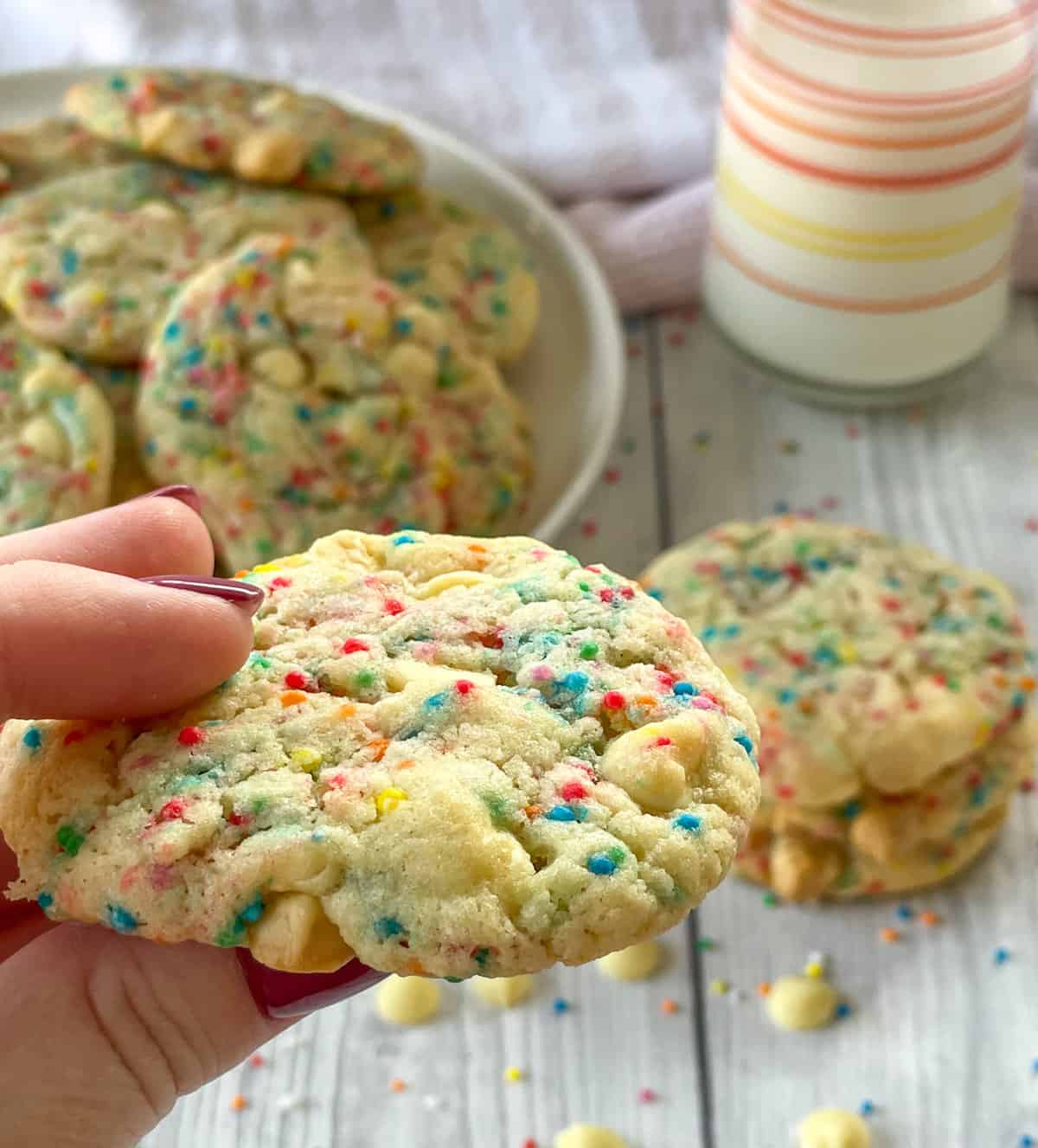 Close up of a hand holding a vanilla cake mix cookie with white chocolate and sprinkles