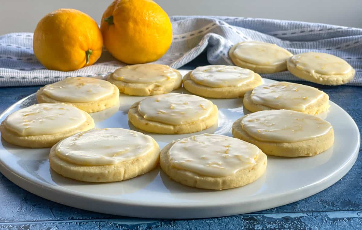 White platter with iced lemon shortbread and two fresh lemons on a blue background