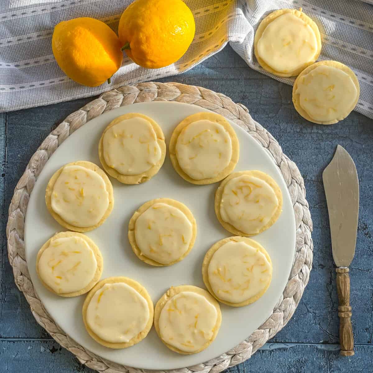 Iced lemon shortbread on a white platter, with fresh lemons and a blue background