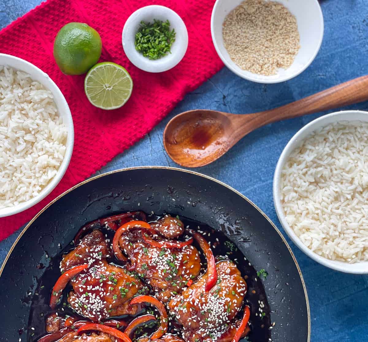 Freshly cooked Sticky Asian Chicken with bowls of rice, chives, sesame seeds and lime juice.