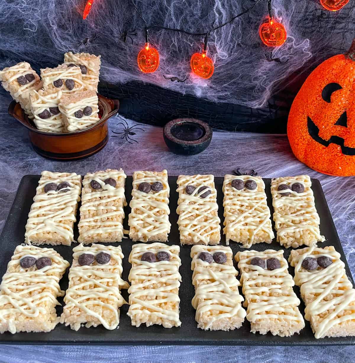 Halloween background decoration with a black plate filled with Rice Krispie Treats shaped like Mummys with white chocolate 