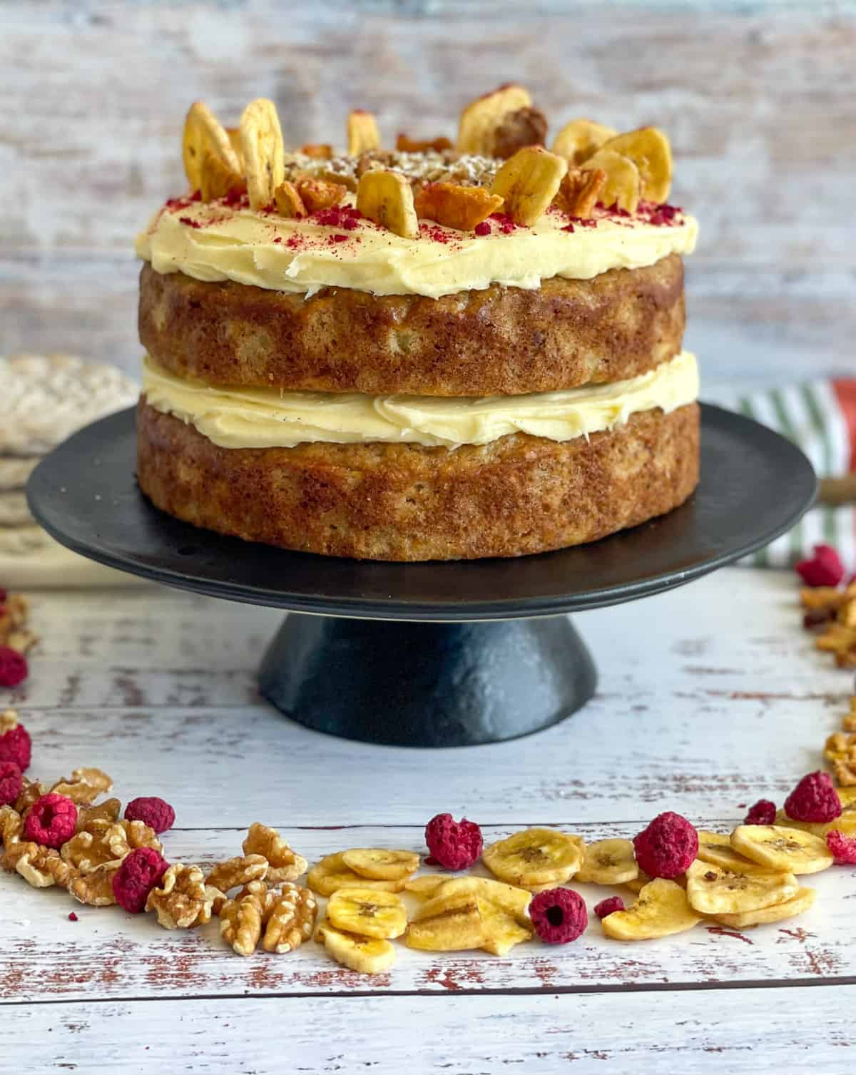 Hummingbird Cake layered with cream cheese frosting and decorated with dried fruits and walnuts on a black cake stand