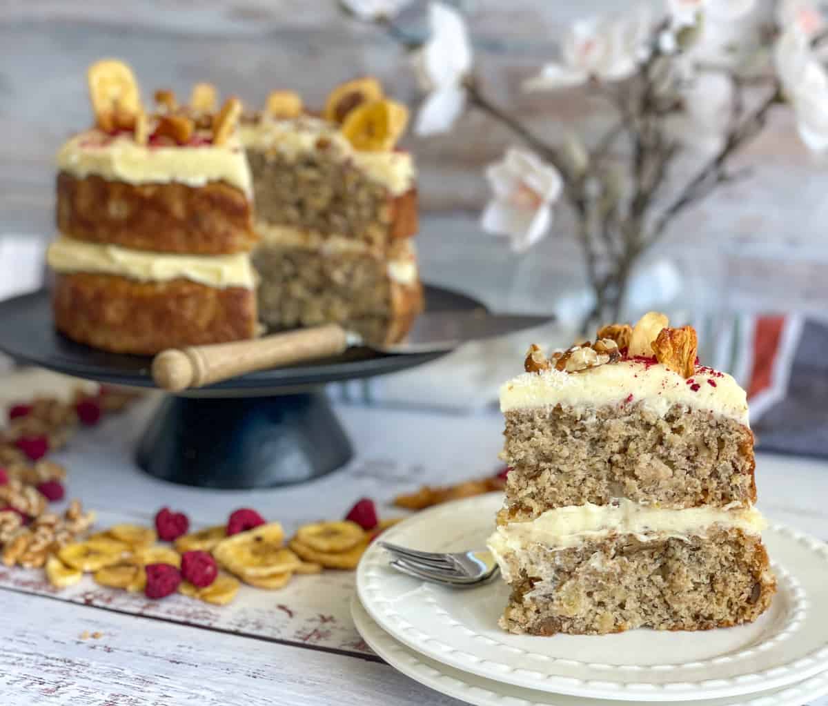 a slice of hummingbird cake on a white side plate with two layers with cream cheese frosting. 