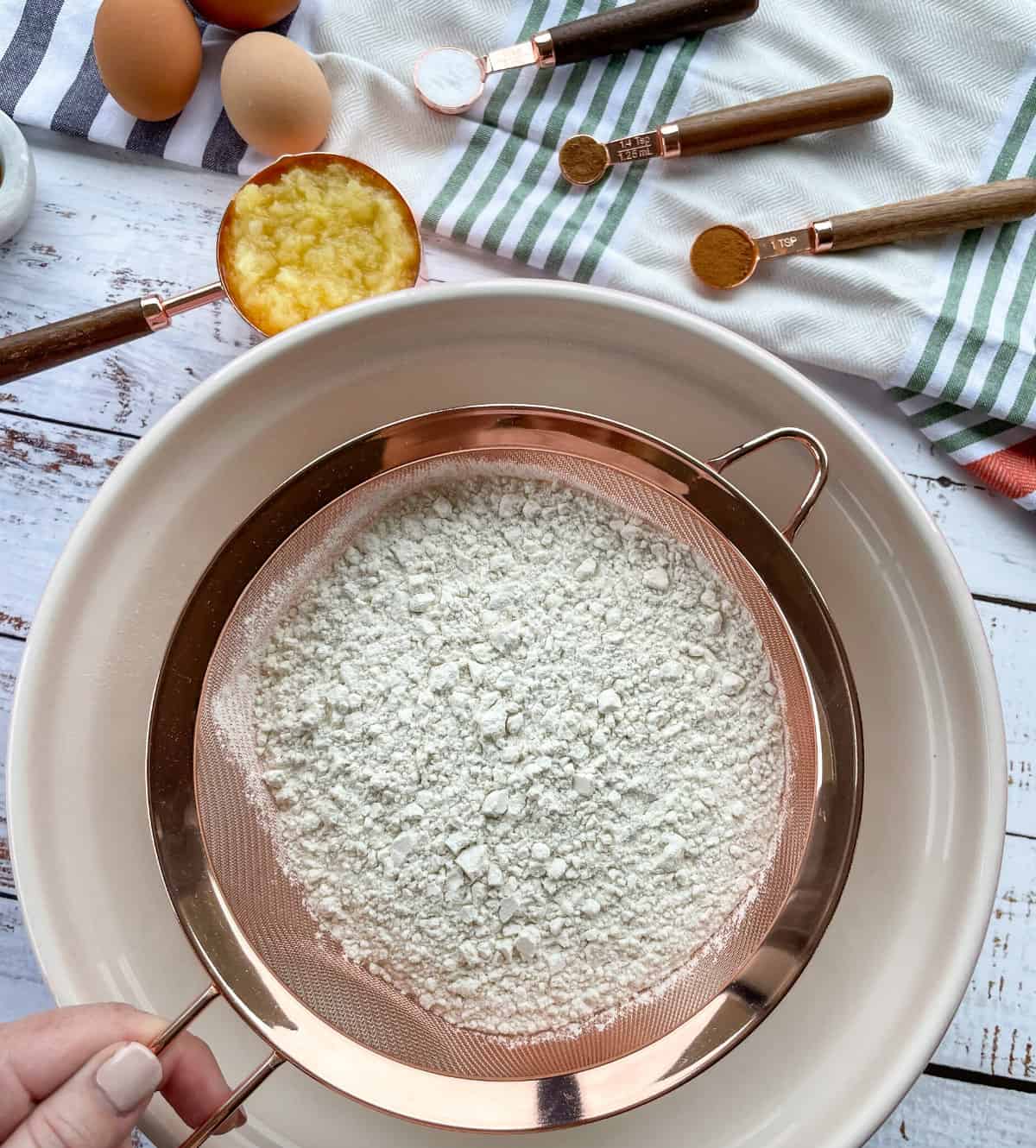 Rose Gold Sift over a large white bowl, with pineapple and measuring spoons in the background. 