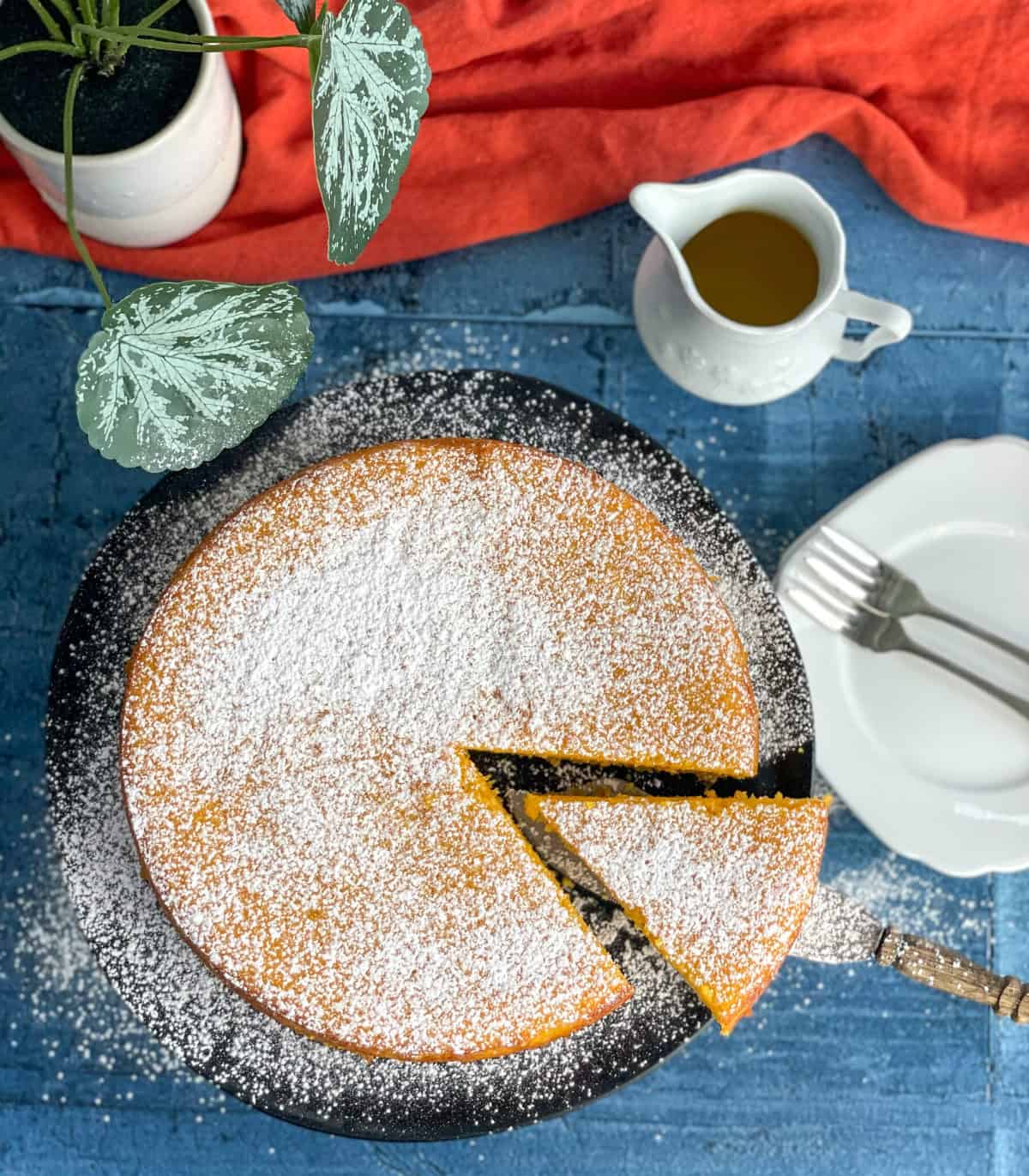 A orange and almond cake on a black cake stand dusted in icing sugar