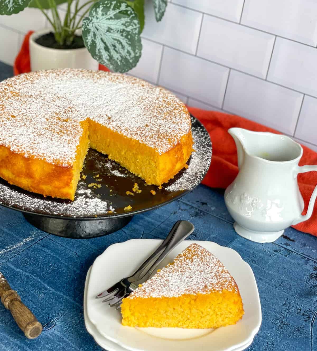 Orange and almond cake, with a slice taken out on a white plate and orange syrup in a small white jug