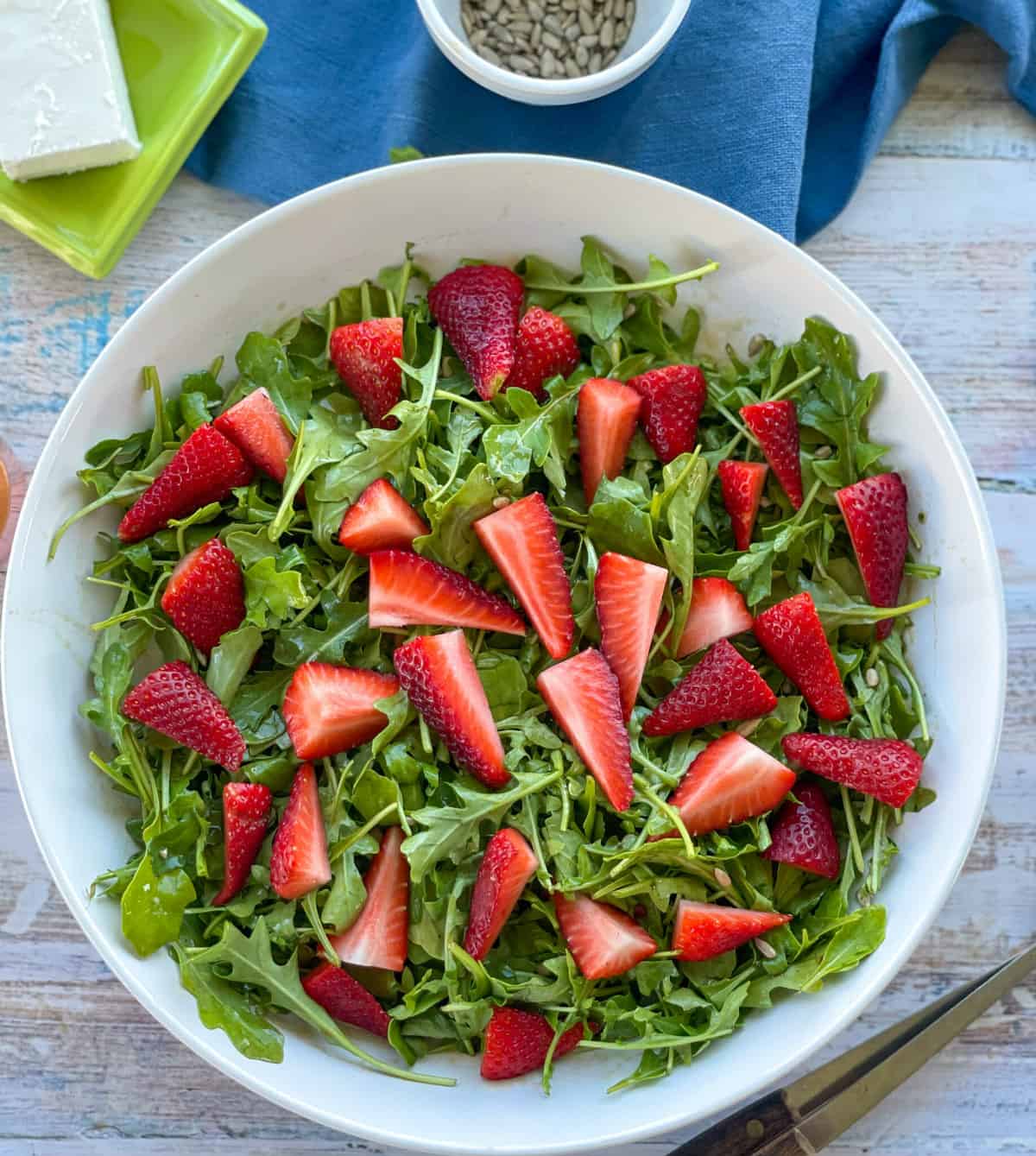 Strawberries placed over salad greens in a white bowl