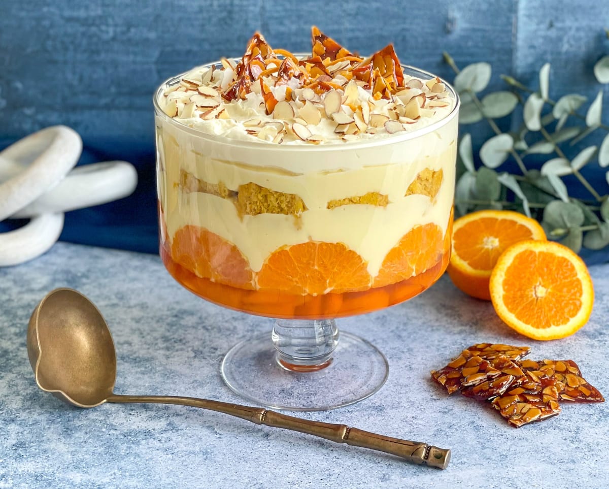 Almond and Orange Trifle, layered in a large glass trifle bowl on a blue background