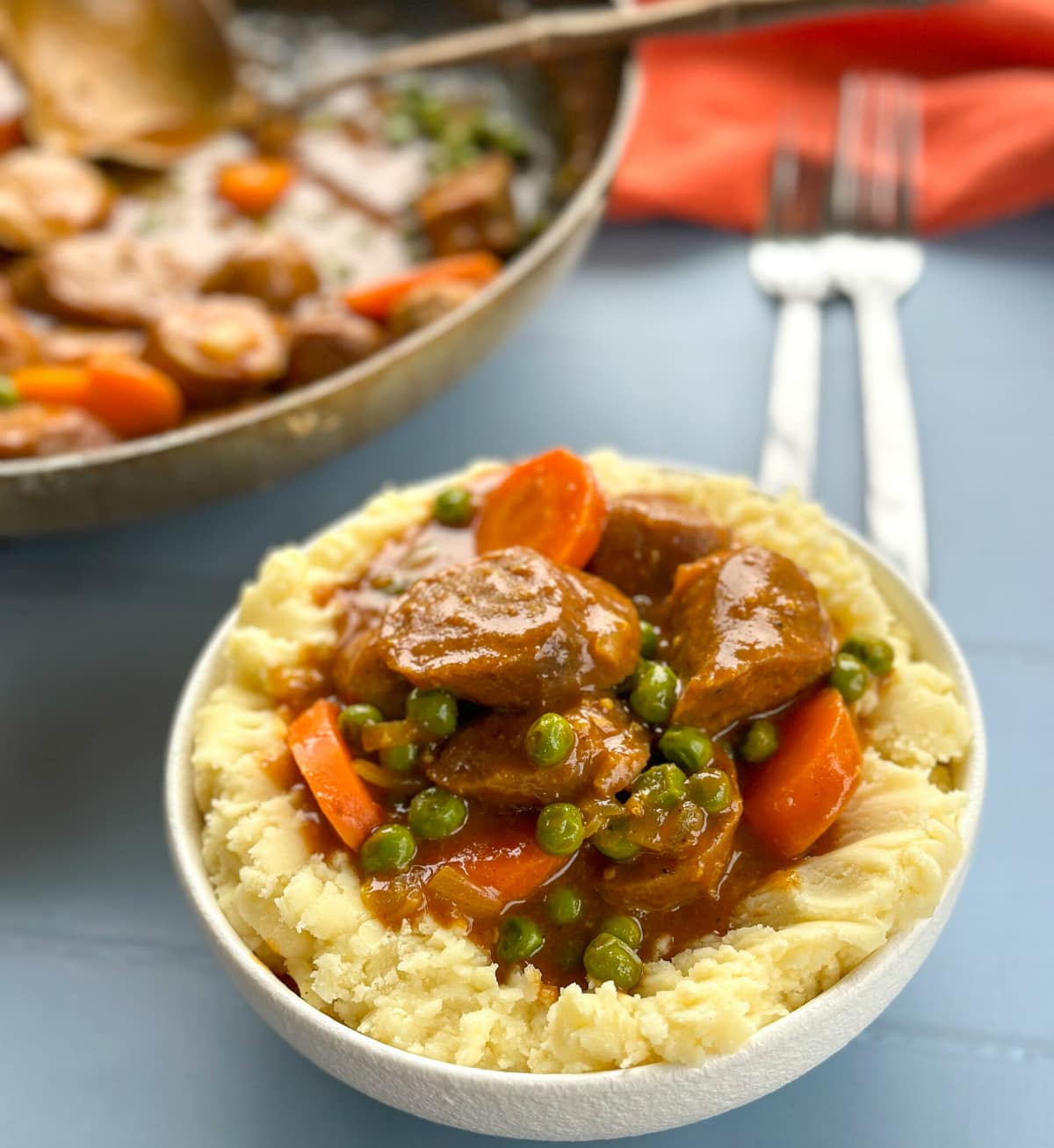 Curried Sausages in a white bowl on mashed potatoes