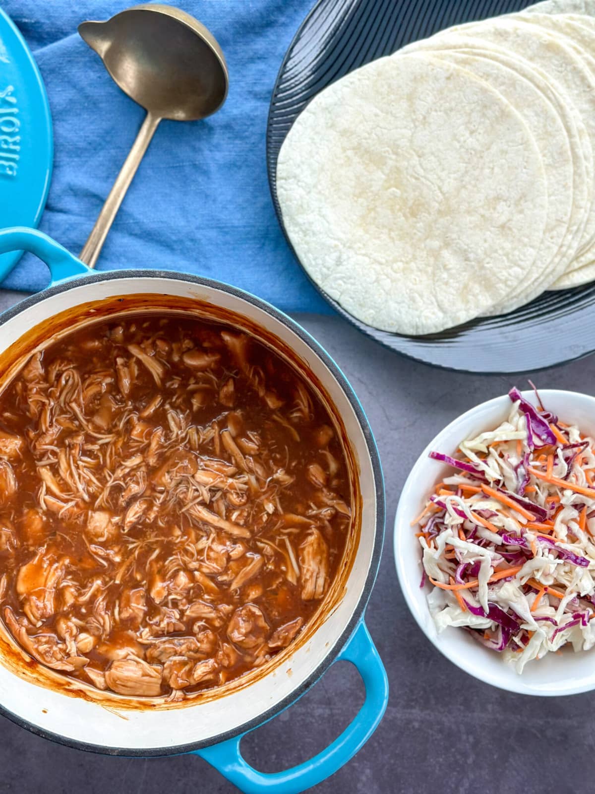 Blue Dutch oven with shredded BBQ Pulled Chicken, coleslaw on the side and soft tacos