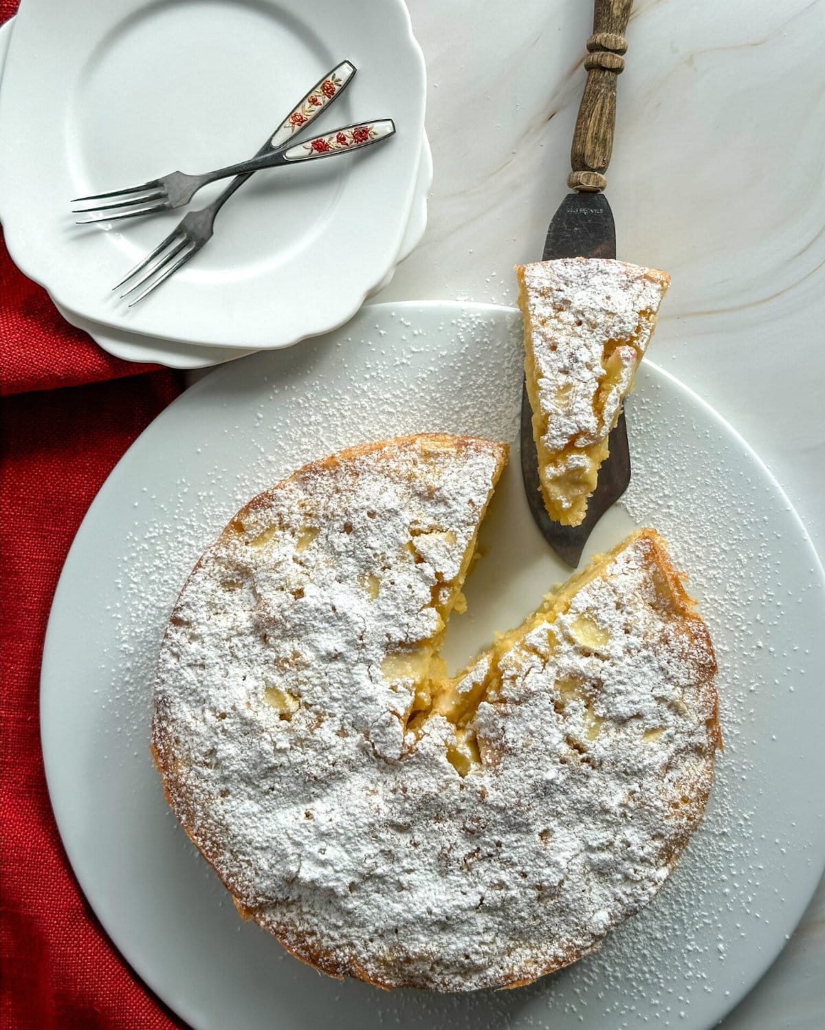 French Apple Cake on a white plate dusted with icing sugar and a slice taken out