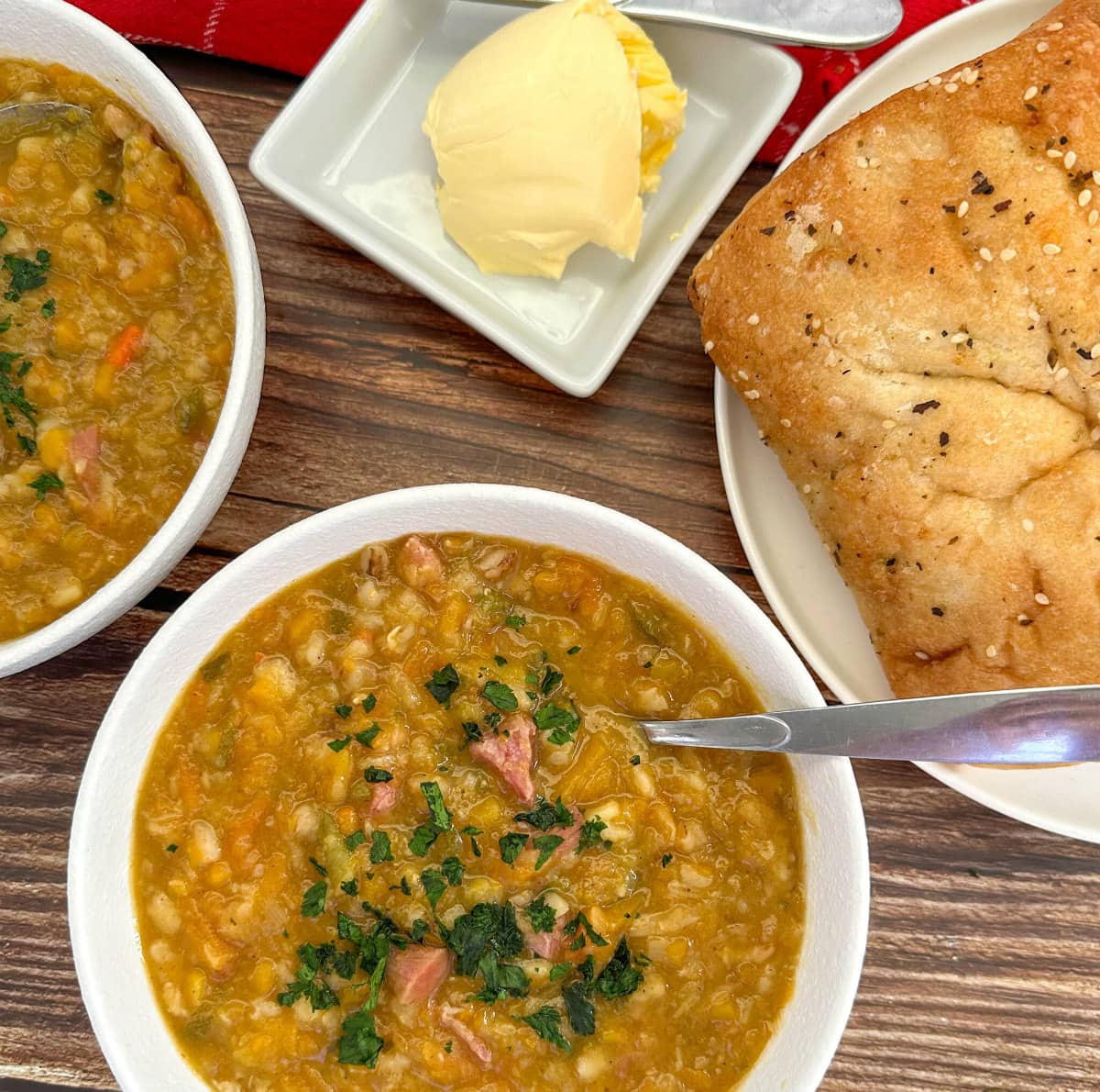 Winter Vegetable and Bacon Hock Soup, in two white bowls served with bread and butter