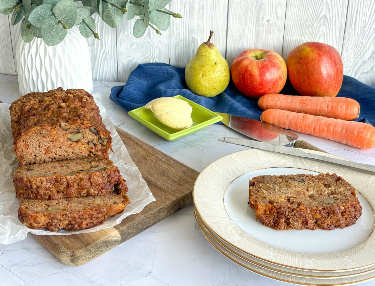 Apple Pear Carrot Loaf with walnuts, a slice on a white plate warmed and smeared with butter