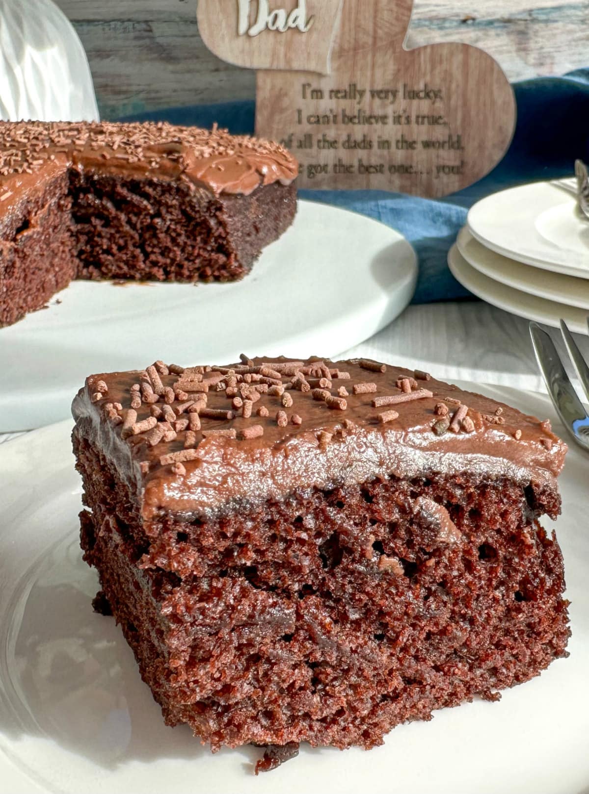 Piece of wacky chocolate cake with chocolate icing on a white plate