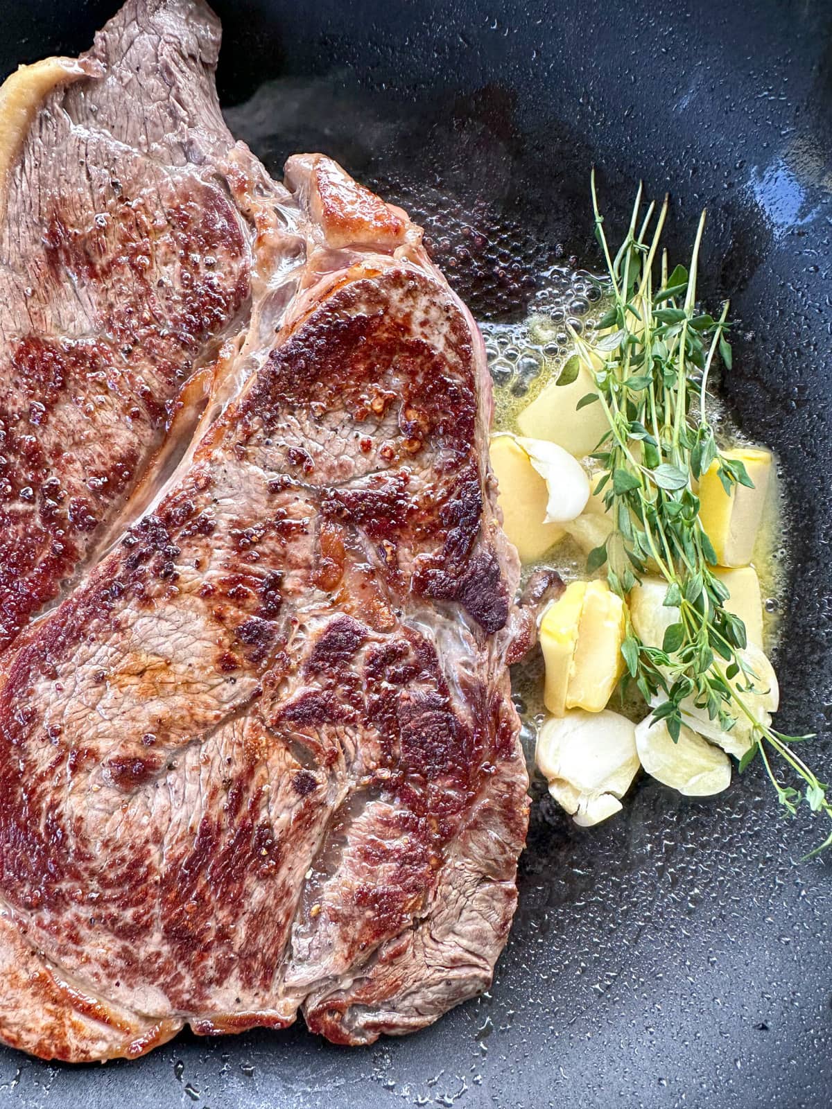 steak in a frying pan with basting liquid of butter, garlic and thyme