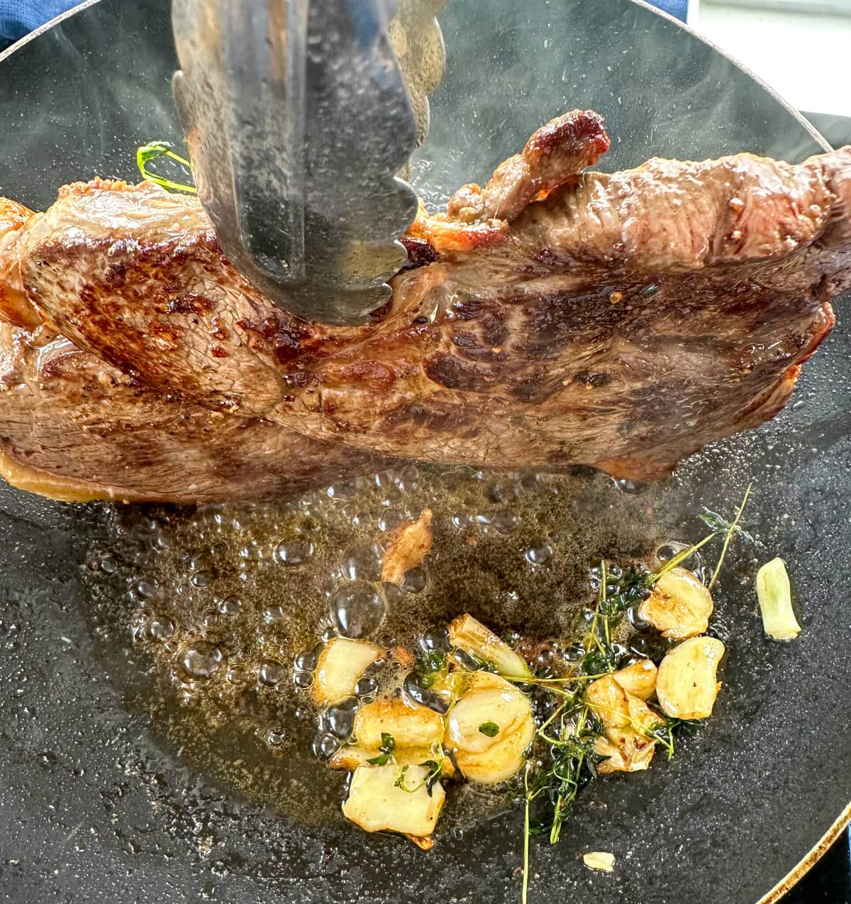 Steak on its side rendering the fat in the pan with butter and garlic