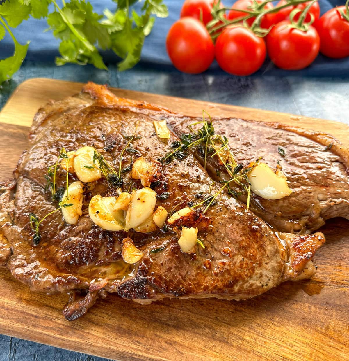 The perfectly cooked rump steak on a wooden board with vine tomatoes in the background