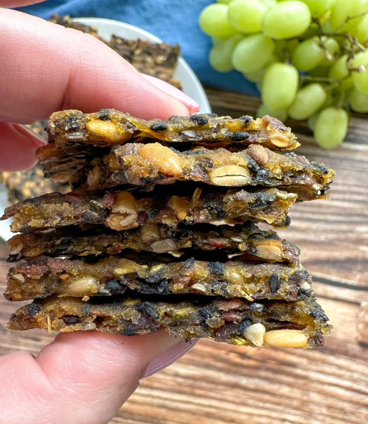 A hand holding a pile of 6 seeded crackers 