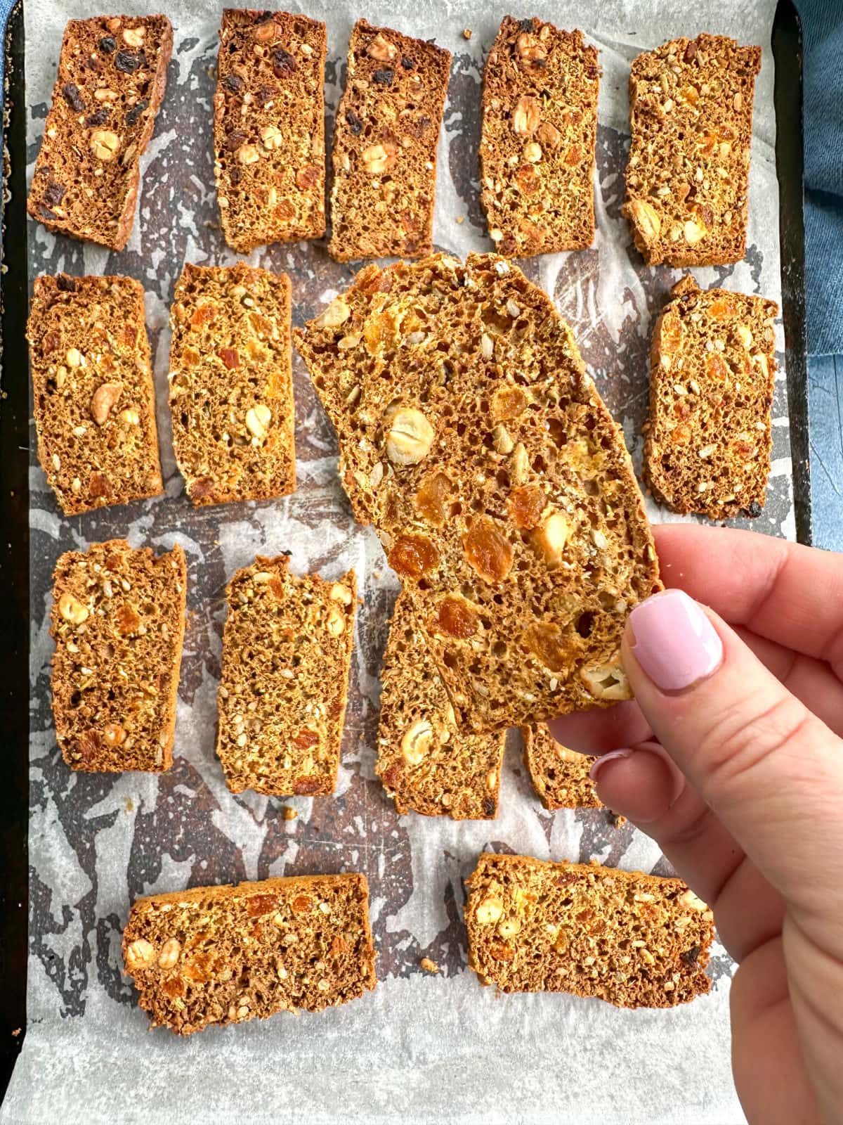 A hand holding a homemade copycat gourmet cracker with apricot, rosemary and cashews