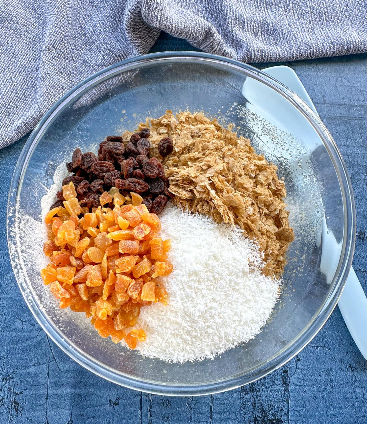 Adding the weetbix, coconut and dried fruit into a glass bowl to make energy bars