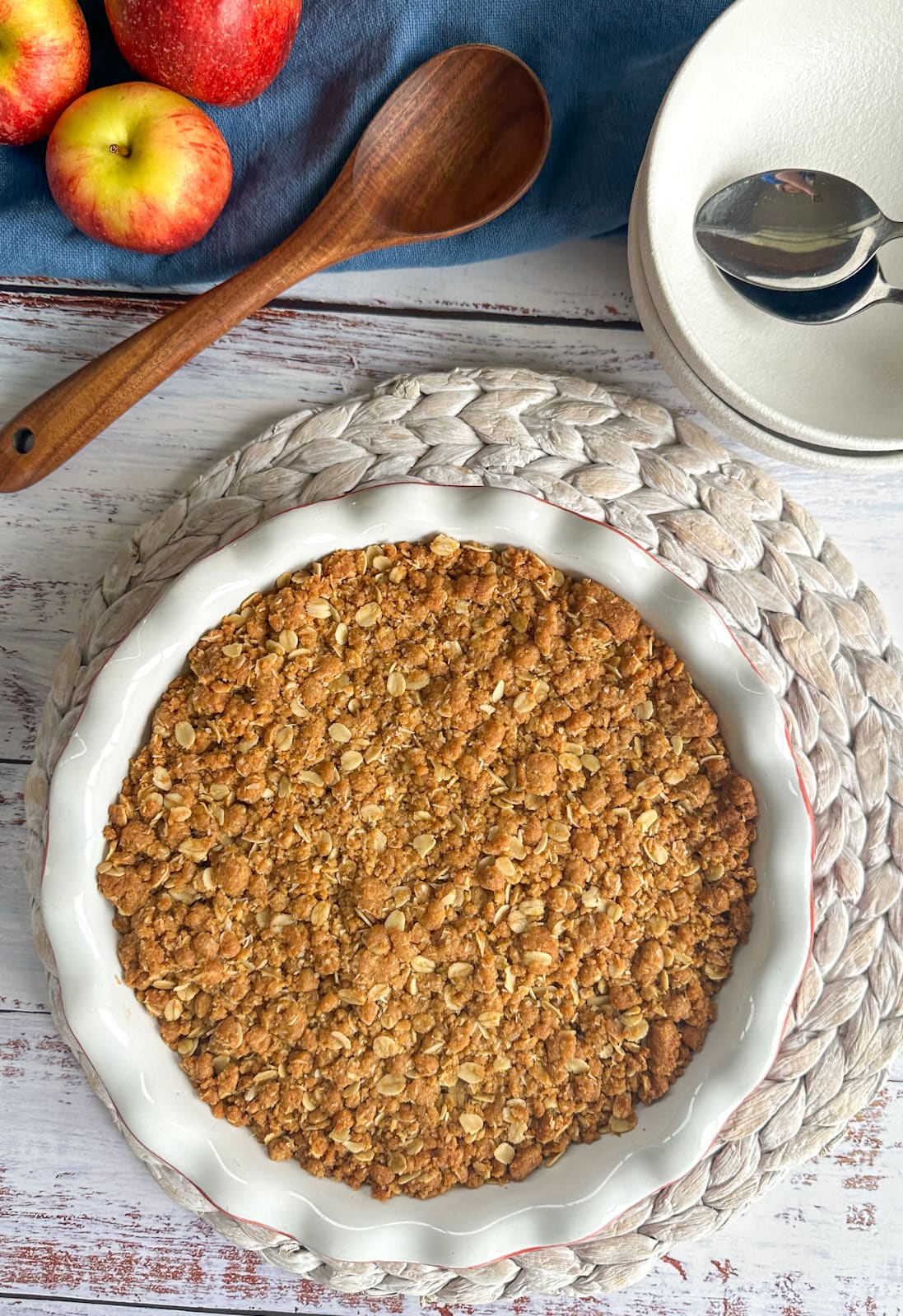 Golden Apple Anzac Crumble freshly baked warm from the oven with fresh apples, a wooden spoon and white bowls ready to serve