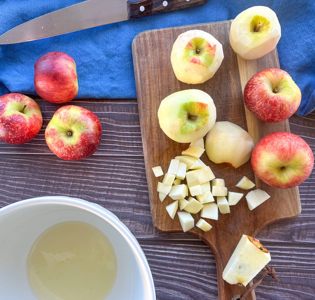 Diced apples and lemon juice for apple pie filling, whole apples, a wooden chopping board and sharp knife
