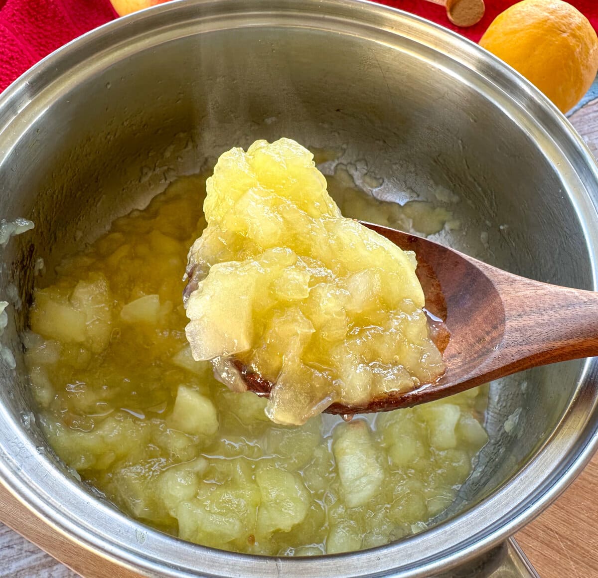 A wooden spoon holding up stewed apples to show the desired consistency