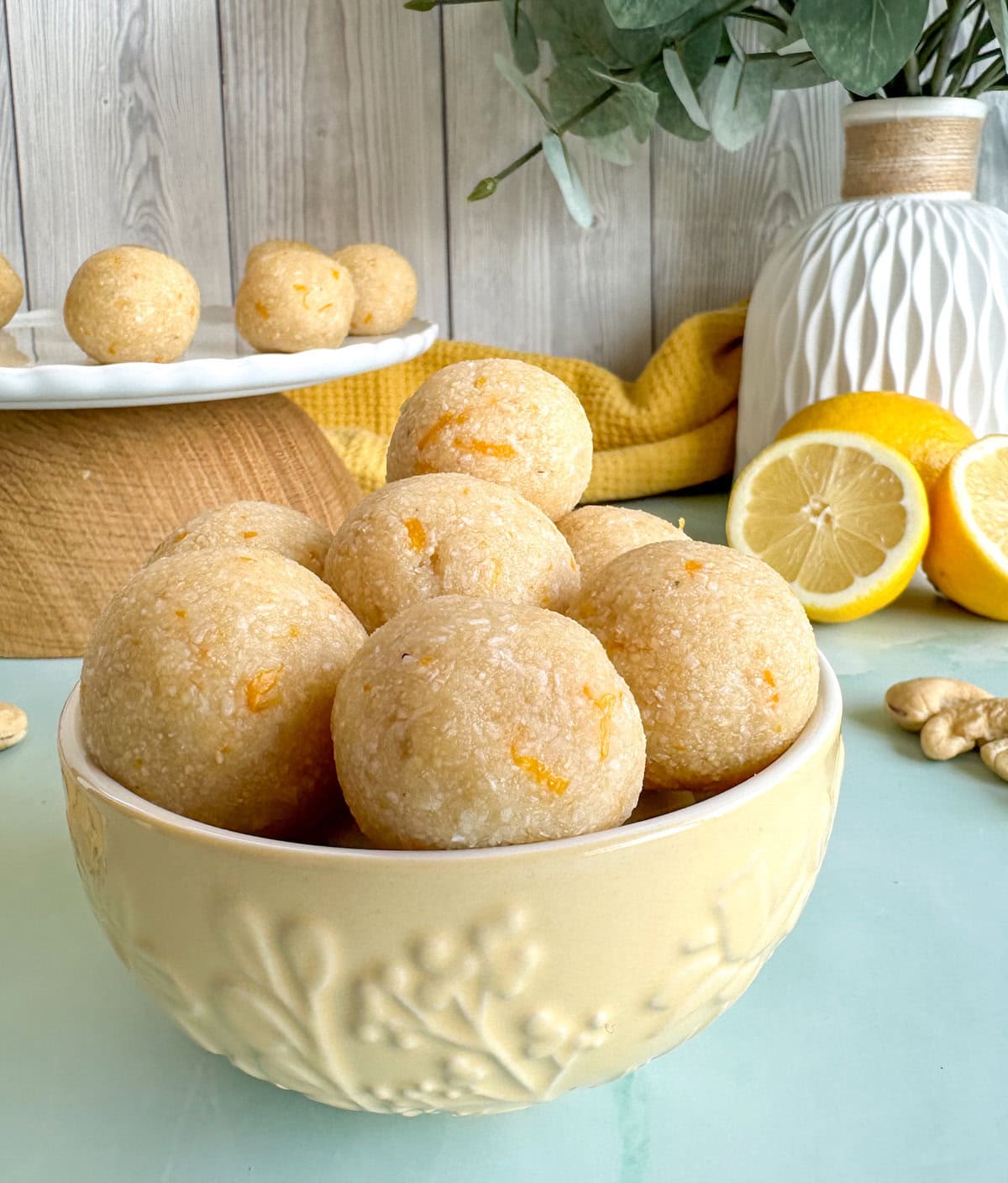 Small yellow bowl holding lemon and cashew bliss balls with fresh lemon